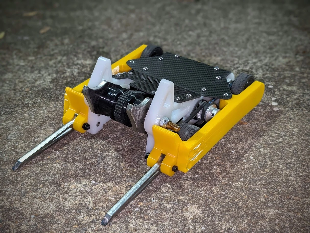 Bubbles, a yellow-and-white combat robot with a black top, front spinning mechanism, and two long metal forks, photographed on concrete.